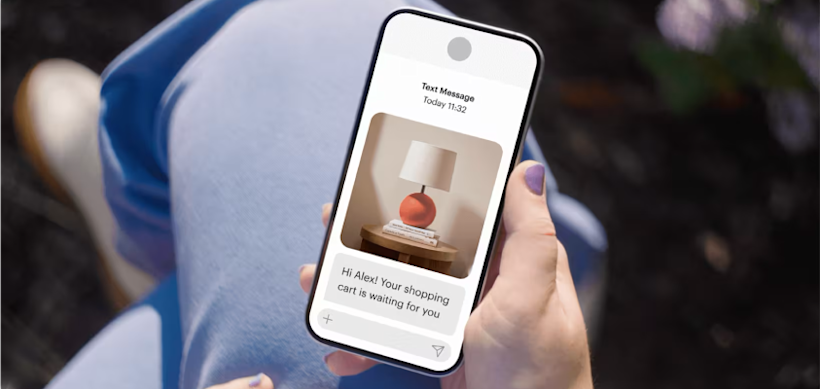 Hand holding smartphone displaying shopping cart reminder message with image of table lamp and decorative apple